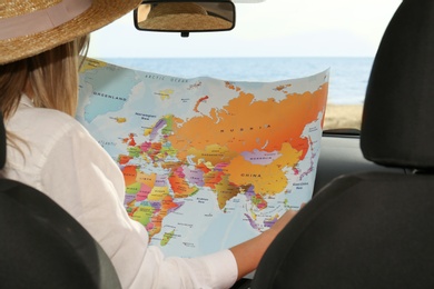 Photo of Young woman with world map in car, back view. Road trip