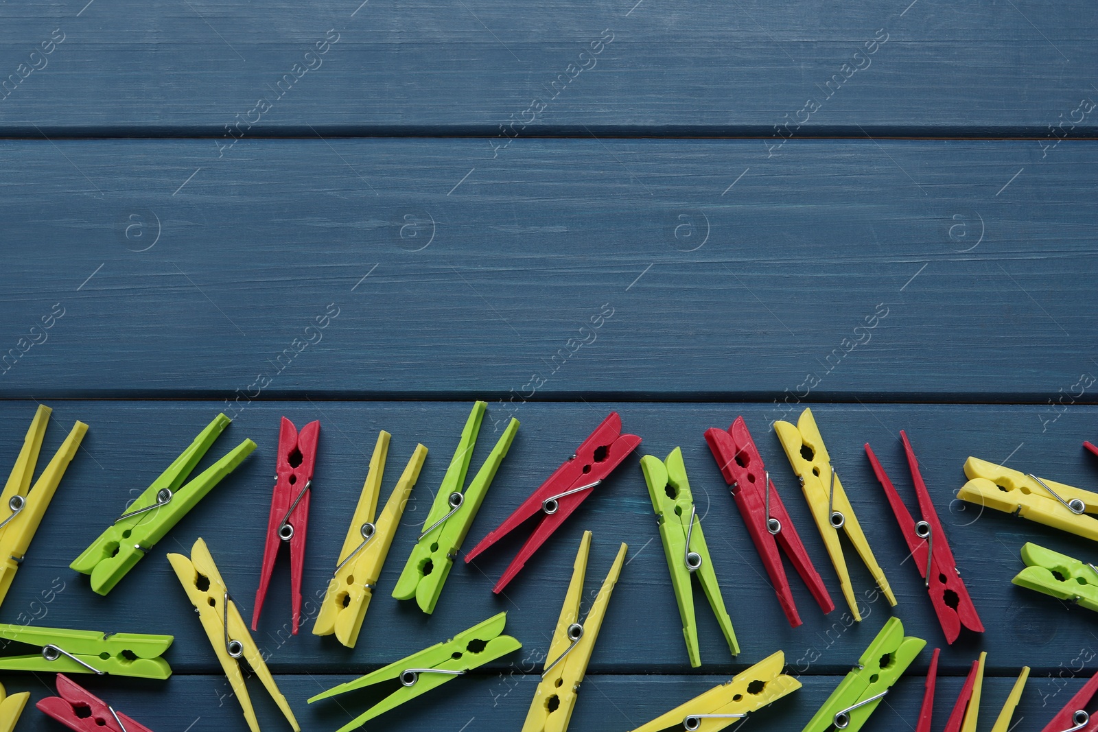 Photo of Colorful plastic clothespins on blue wooden background, flat lay. Space for text