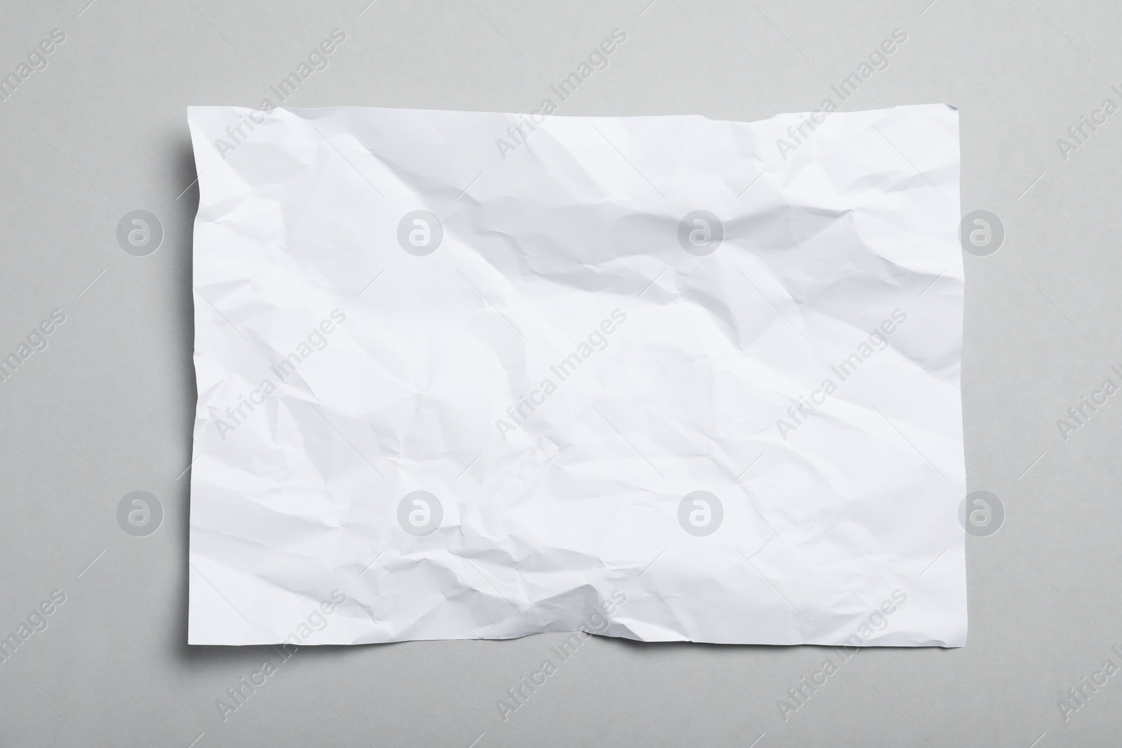 Photo of Sheet of white crumpled paper on grey background, top view