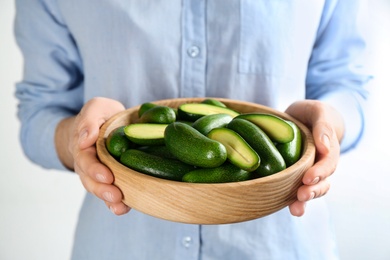 Photo of Woman holding wooden bowl with fresh seedless avocados, closeup