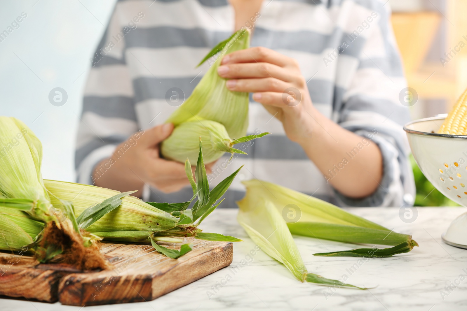 Photo of Woman husking corn at table, focus on hands