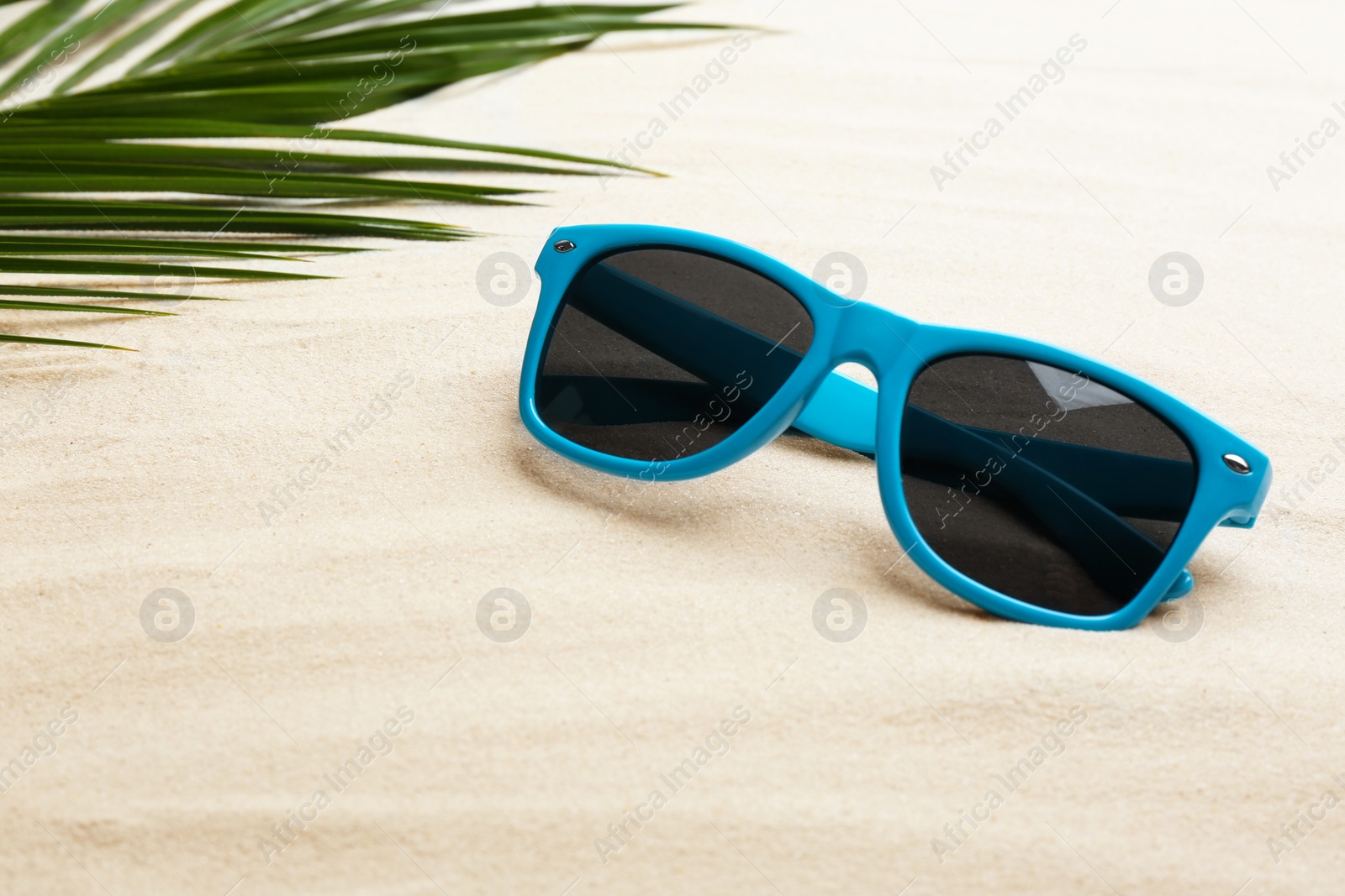 Photo of Stylish sunglasses and tropical leaf on white sand, space for text. Vacation time