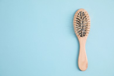 Photo of Wooden brush with lost hair on light blue background, top view. Space for text