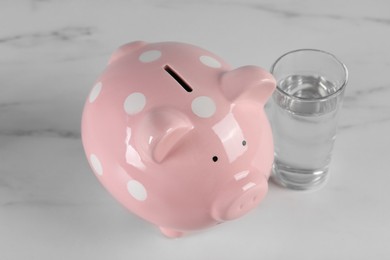 Water scarcity concept. Piggy bank and glass of drink on white marble table