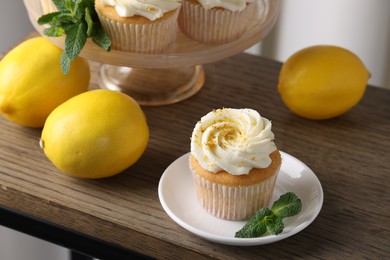 Photo of Delicious lemon cupcakes with white cream, mint and lemons on wooden table, closeup