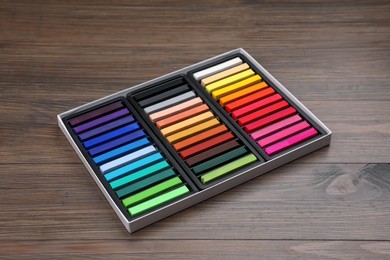 Photo of Set of colorful pastels in box on wooden table. Drawing materials