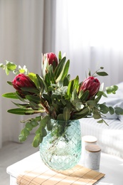Photo of Vase with bouquet of beautiful Protea flowers on white table in bedroom