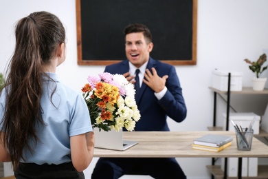 Photo of Schoolgirl with bouquet congratulating her  emotional pedagogue in classroom. Teacher's day