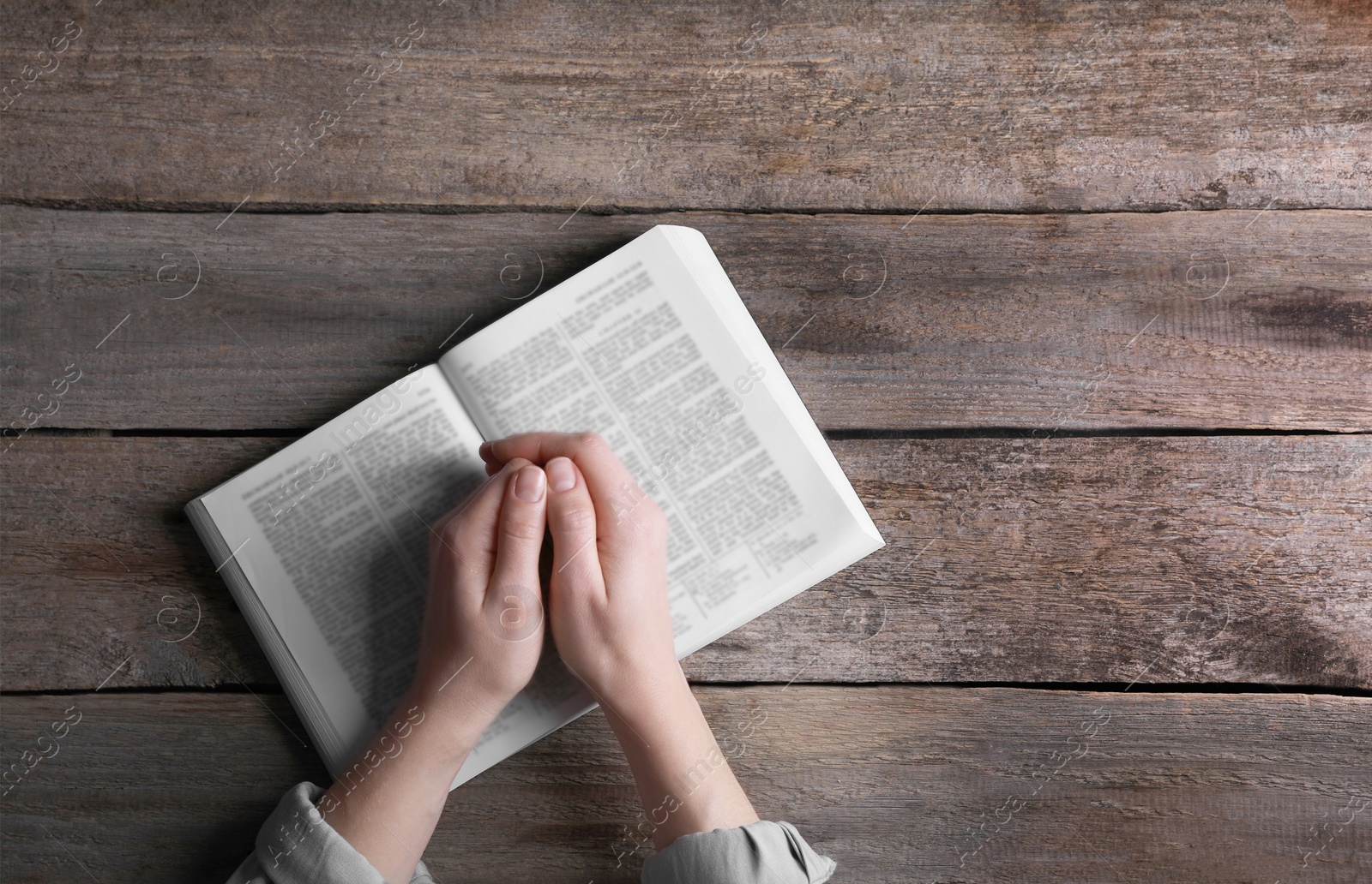 Photo of Religion. Christian woman praying over Bible at wooden table, top view. Space for text