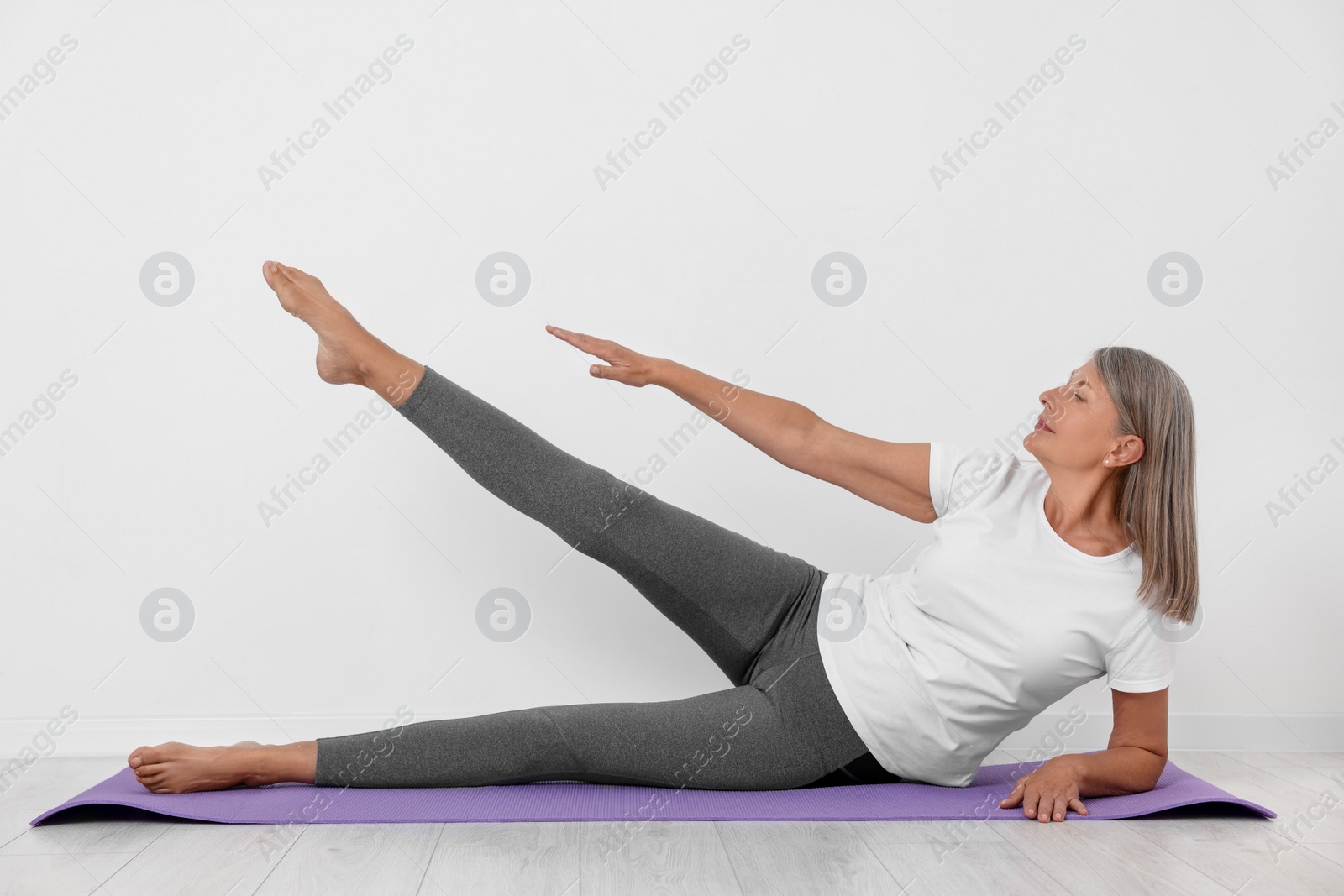 Photo of Senior woman practicing yoga on mat near white wall