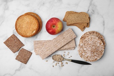 Photo of Rye crispbreads, rice cakes and rusks on white marble table, flat lay