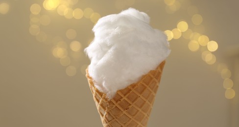 Sweet cotton candy in waffle cone against blurred lights, closeup