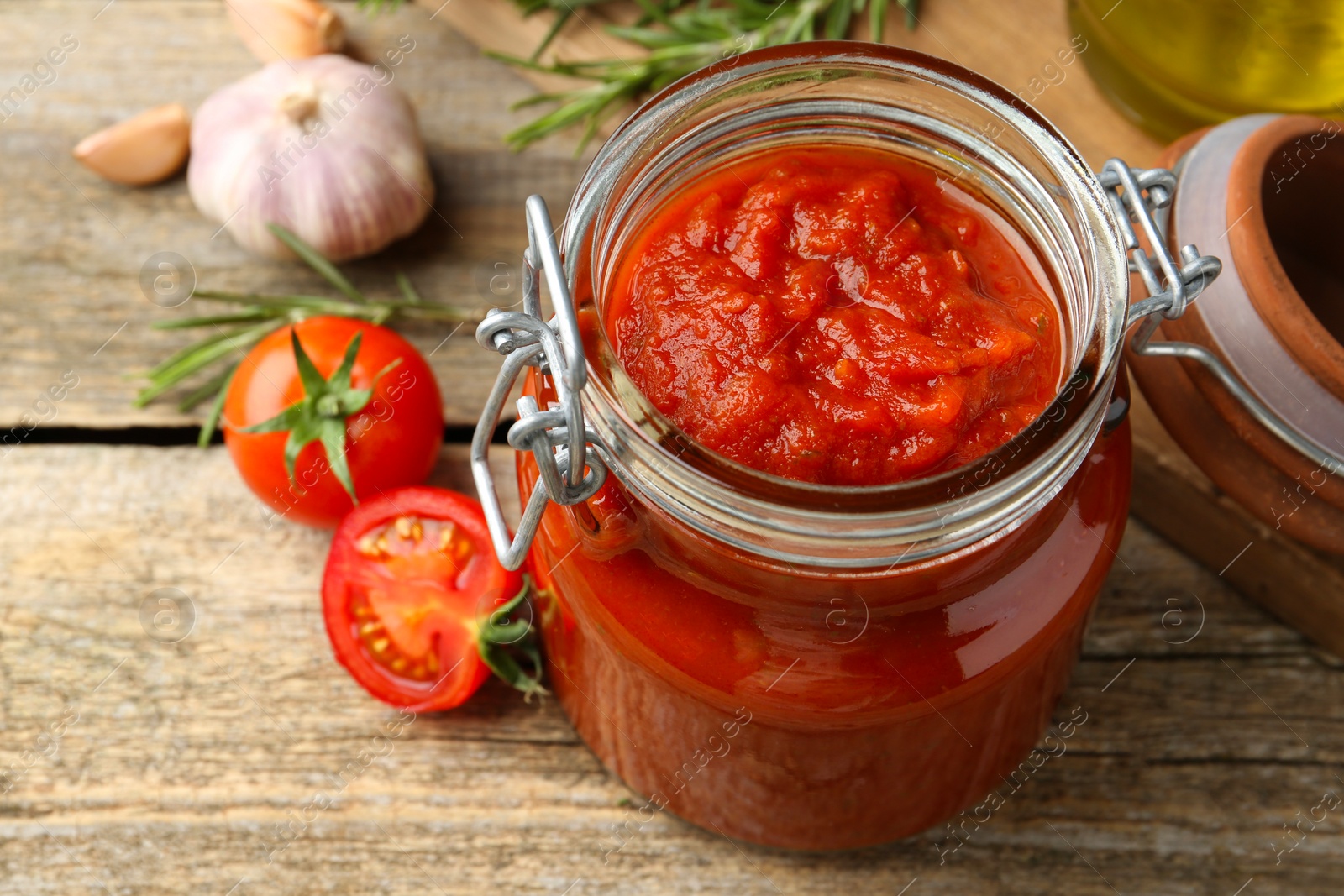 Photo of Homemade tomato sauce in jar and fresh ingredients on wooden table, closeup