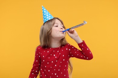 Cute little girl in party hat with blower on yellow background