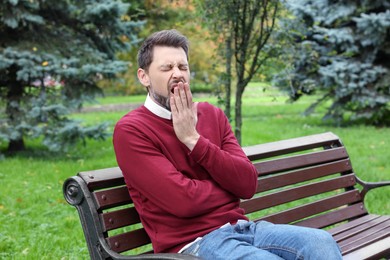 Sleepy tired man yawning on bench in beautiful green park