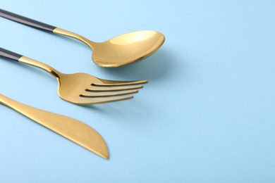 Photo of Stylish golden cutlery set on light blue background, closeup. Space for text