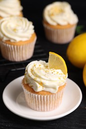 Photo of Delicious lemon cupcakes with white cream on black table, closeup