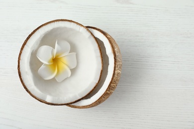 Halves of coconut and flower on white wooden background, top view. Space for text