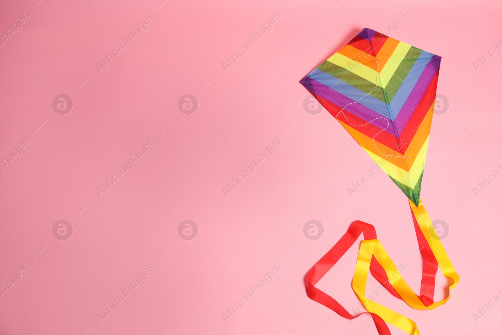 Photo of Bright rainbow kite on pink background, top view. Space for text