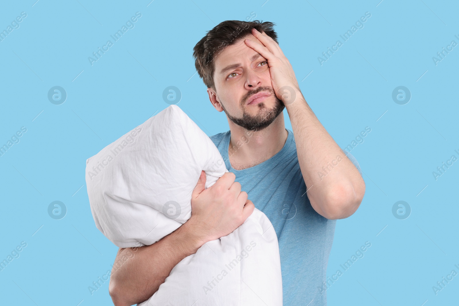 Photo of Tired man with pillow on light blue background. Insomnia problem