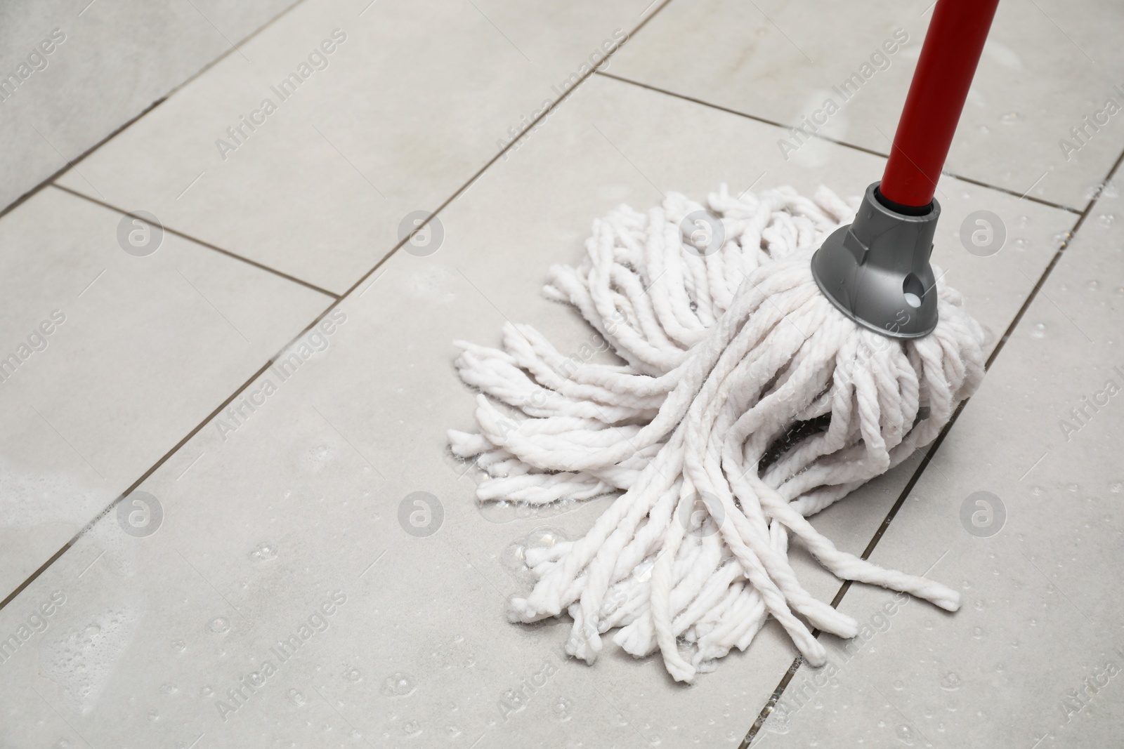 Photo of Cleaning grey tiled floor with string mop, space for text