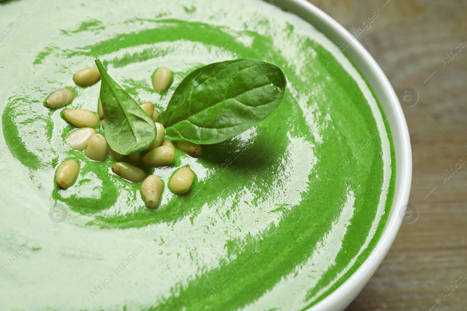 Photo of Bowl of healthy green soup with fresh spinach on wooden table, closeup view