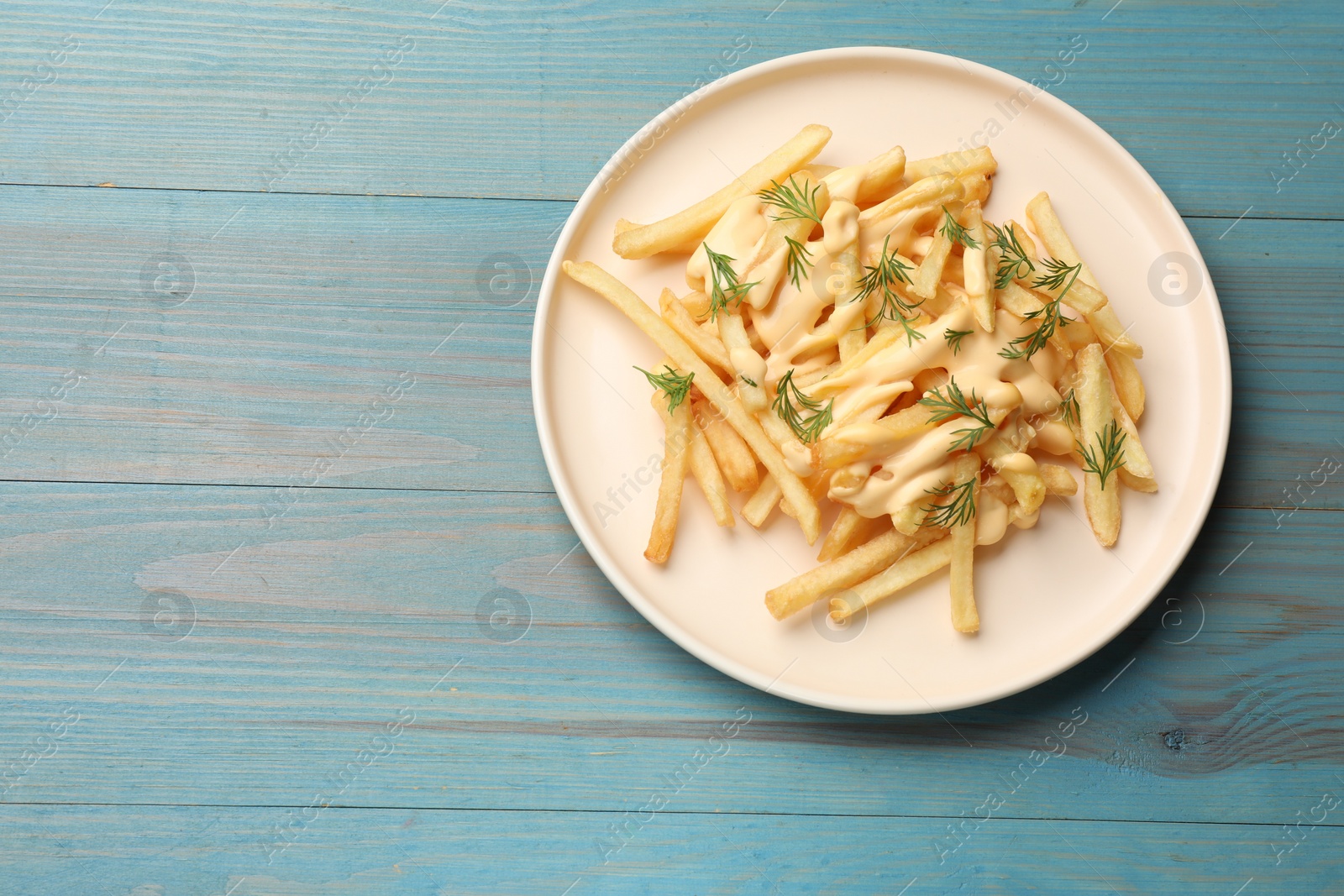 Photo of Delicious french fries with cheese sauce and dill on light blue wooden table, top view. Space for text