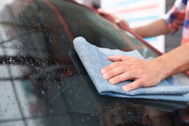 Photo of Man cleaning windshield with duster, closeup. Car wash service