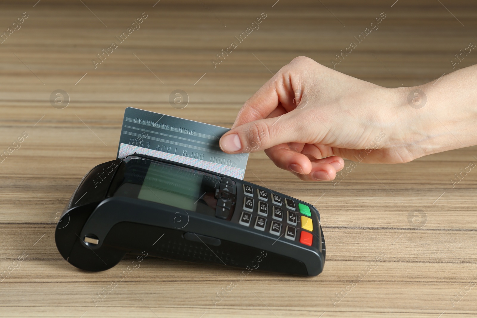 Photo of Woman with credit card using modern payment terminal at wooden table, closeup