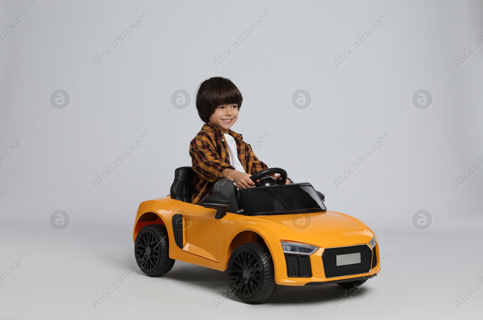 Photo of Cute little boy driving children's electric toy car on grey background