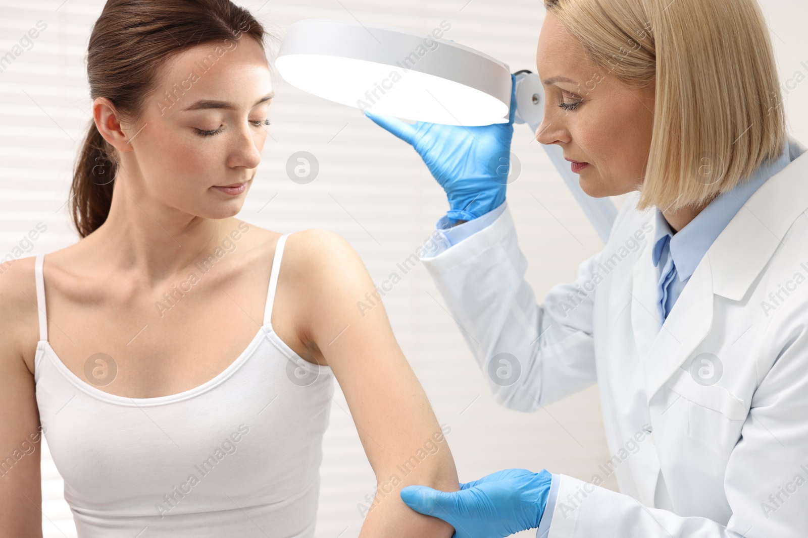 Photo of Dermatologist examining patient under lamp in clinic