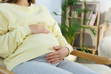 Photo of Pregnant woman touching belly in living room, closeup