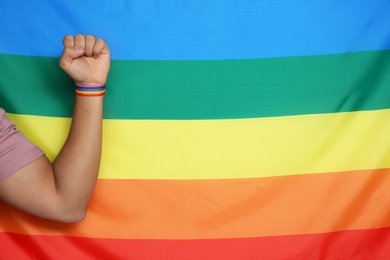 Man wearing gay wristband on hand near rainbow flag, closeup. Space for text