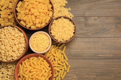 Photo of Different types of pasta on wooden table, flat lay. Space for text