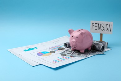 Photo of Pension savings. Piggy bank, cash and graphs on light blue background