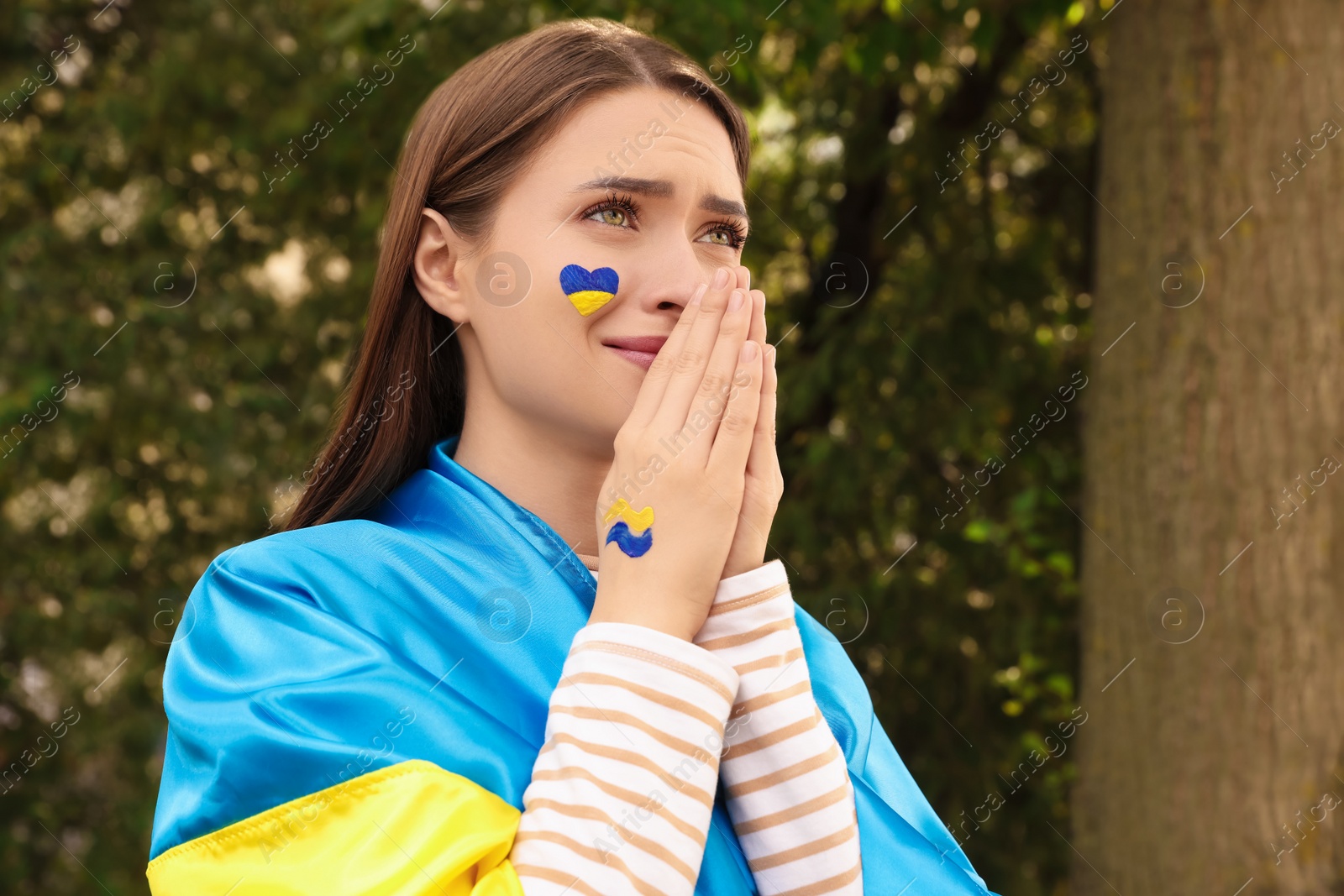 Photo of Emotional young Ukrainian woman with clasped hands outdoors, space for text