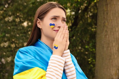 Emotional young Ukrainian woman with clasped hands outdoors, space for text