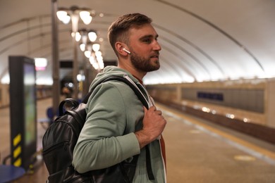 Photo of Young man with backpack and earphones at subway station. Public transport