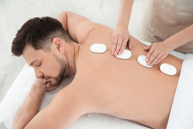 Handsome man receiving hot stone massage in spa salon