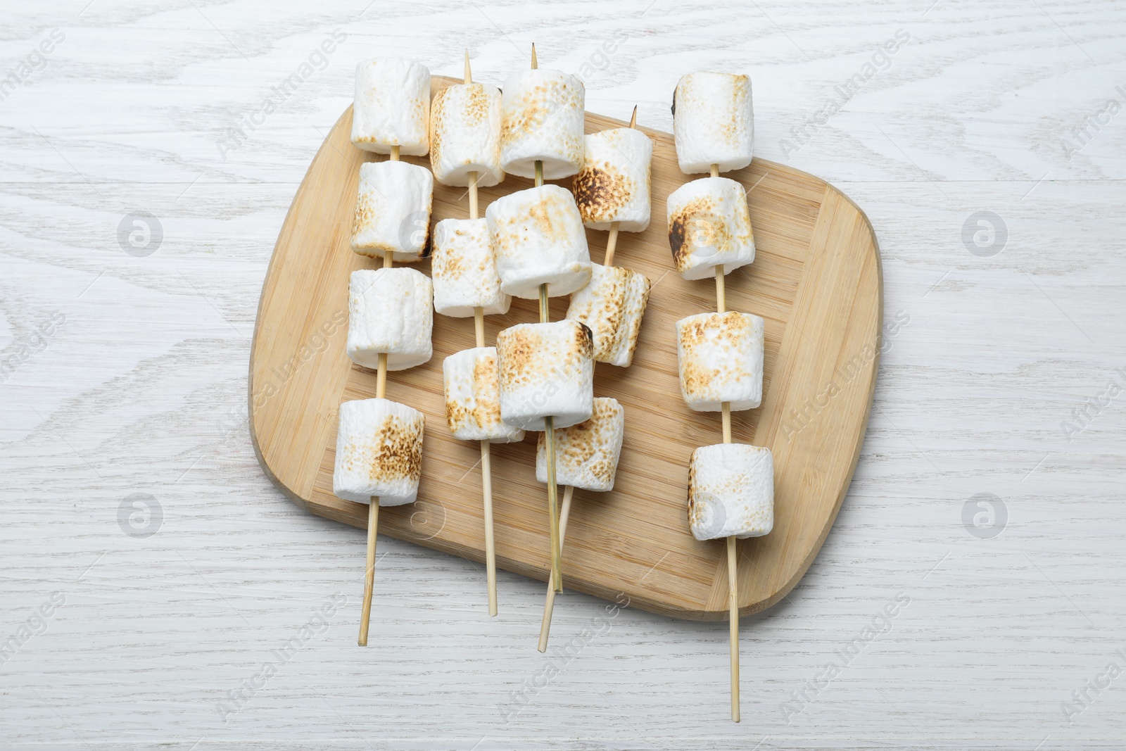 Photo of Sticks with roasted marshmallows on white wooden table, top view