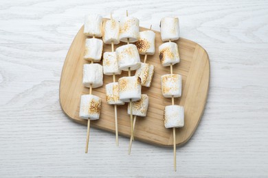 Sticks with roasted marshmallows on white wooden table, top view