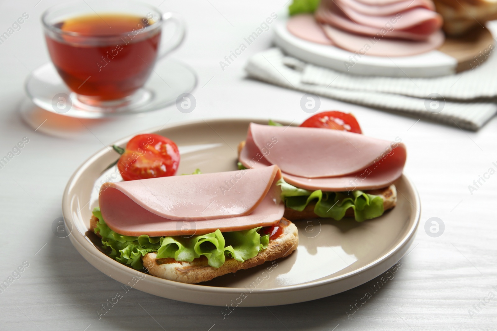 Photo of Plate of tasty sandwiches with boiled sausage, tomato and lettuce on white wooden table