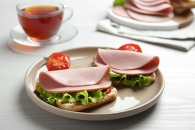 Plate of tasty sandwiches with boiled sausage, tomato and lettuce on white wooden table