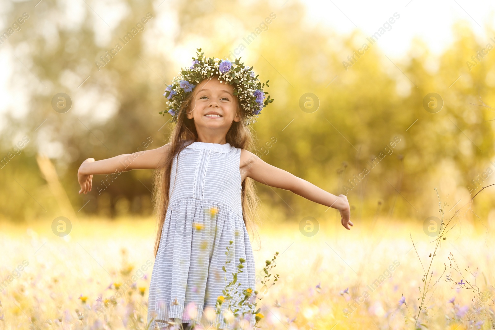 Photo of Cute little girl wearing flower wreath outdoors. Child spending time in nature