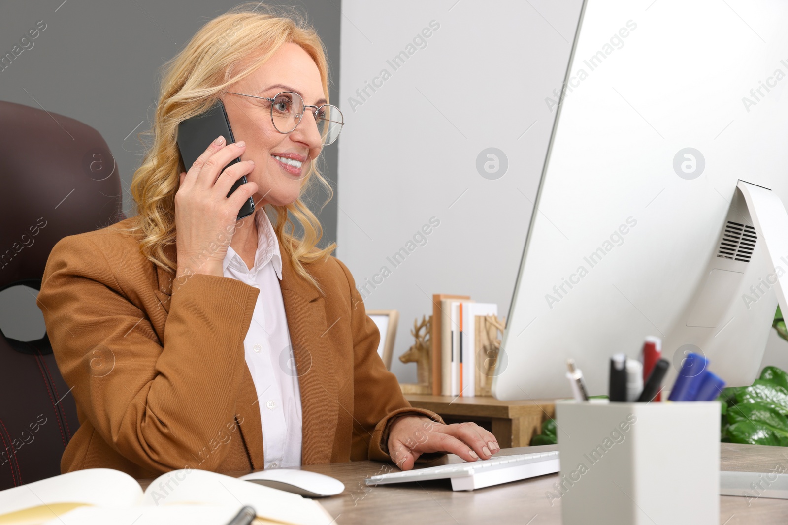 Photo of Lady boss talking on smartphone near computer at desk in office. Successful businesswoman