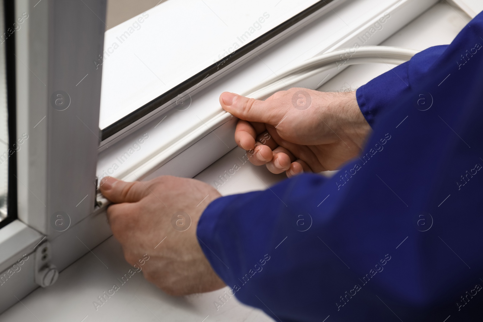 Photo of Worker putting rubber draught strip onto window indoors, closeup