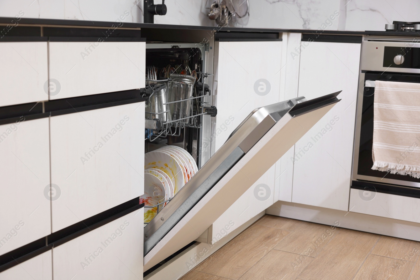 Photo of Open modern dishwasher with dirty tableware in kitchen