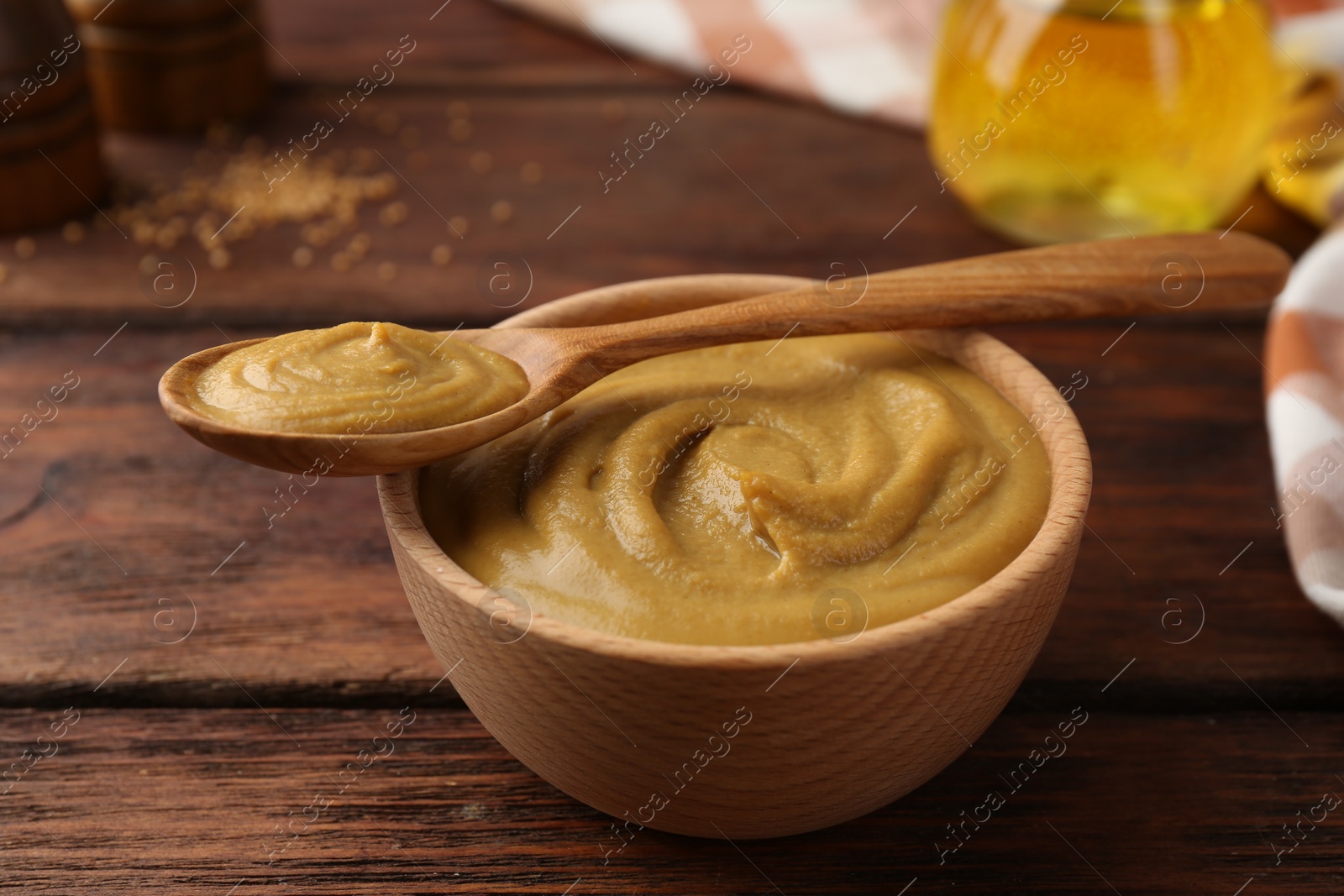 Photo of Bowl and spoon with tasty mustard sauce on wooden table, closeup