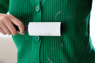 Woman removing hair from green knitted jacket with lint roller on light background, closeup