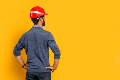 Photo of Professional engineer in hard hat on yellow background, back view. Space for text